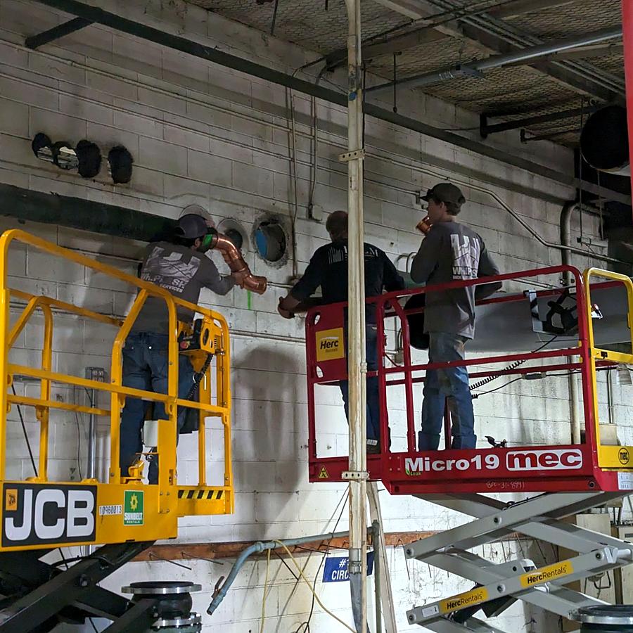 Our crew fitting copper piping from scissor lifts inside a plant