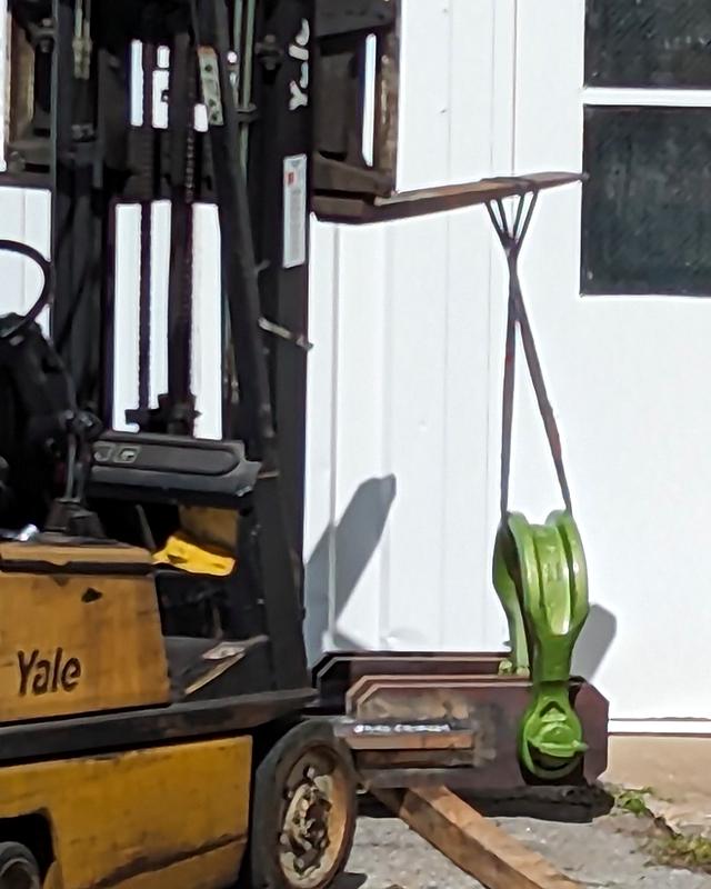 A forklift holding the adapter's giant green shackle on its plate
